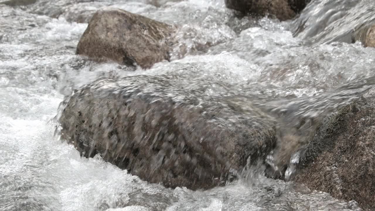 山涧从岩石下流入河床。冷水在岩石上沸腾。湍急的水流成瀑布状流动，形成泡沫和飞溅。视频素材