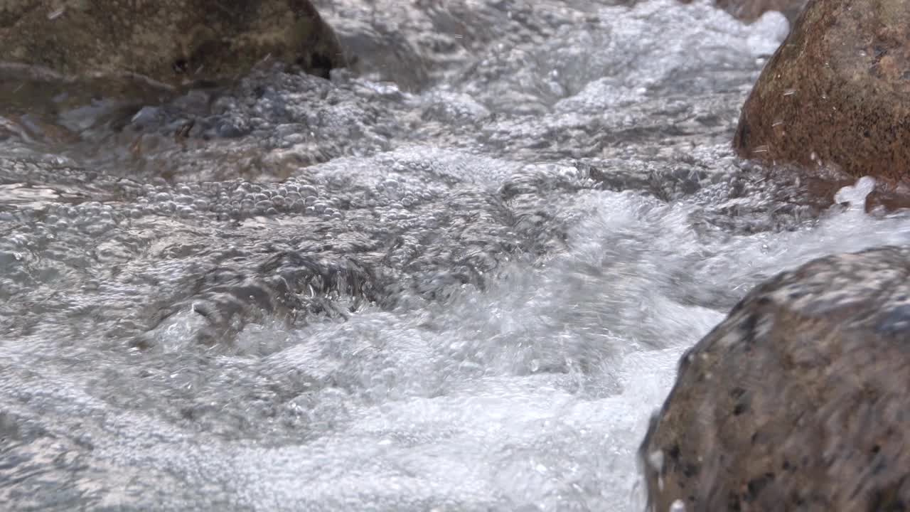 水在三个巨石之间沸腾。河流特写，泡沫和泡沫从快速流动。溪水绕着石头流，从石头上飞溅而下。视频素材