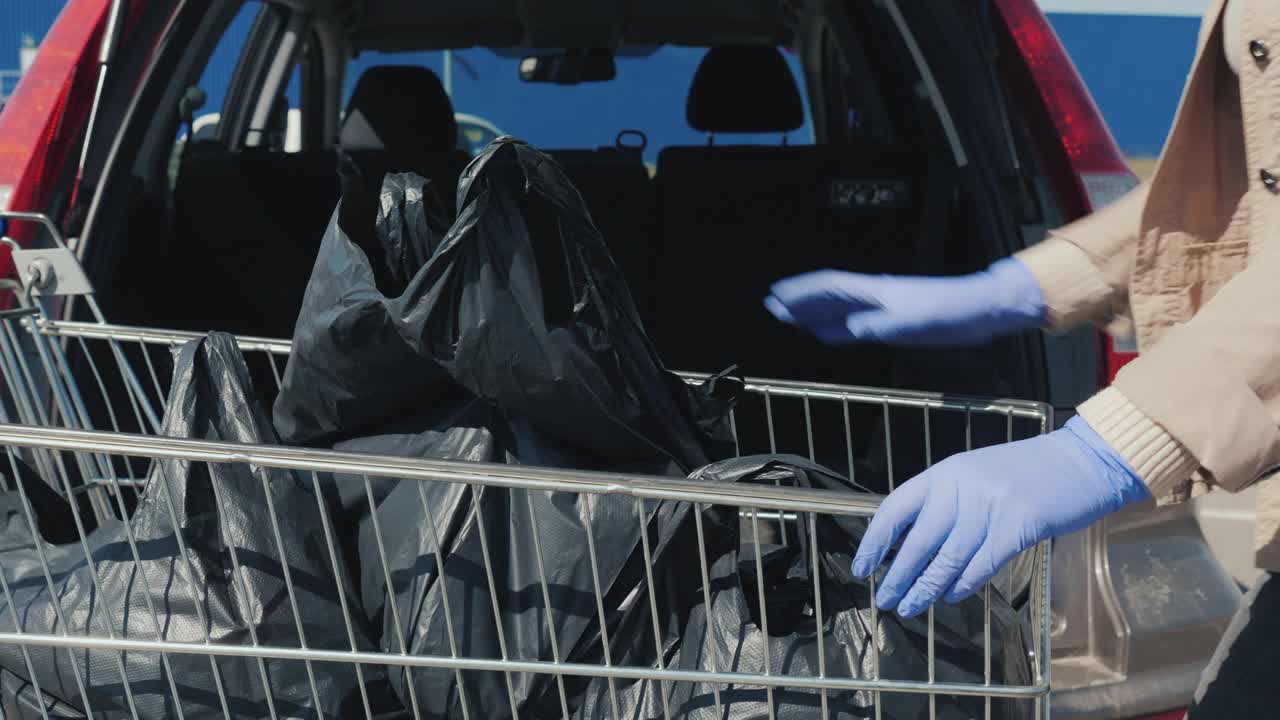 戴着防护手套的男人把购物袋放在汽车的后备箱里视频素材