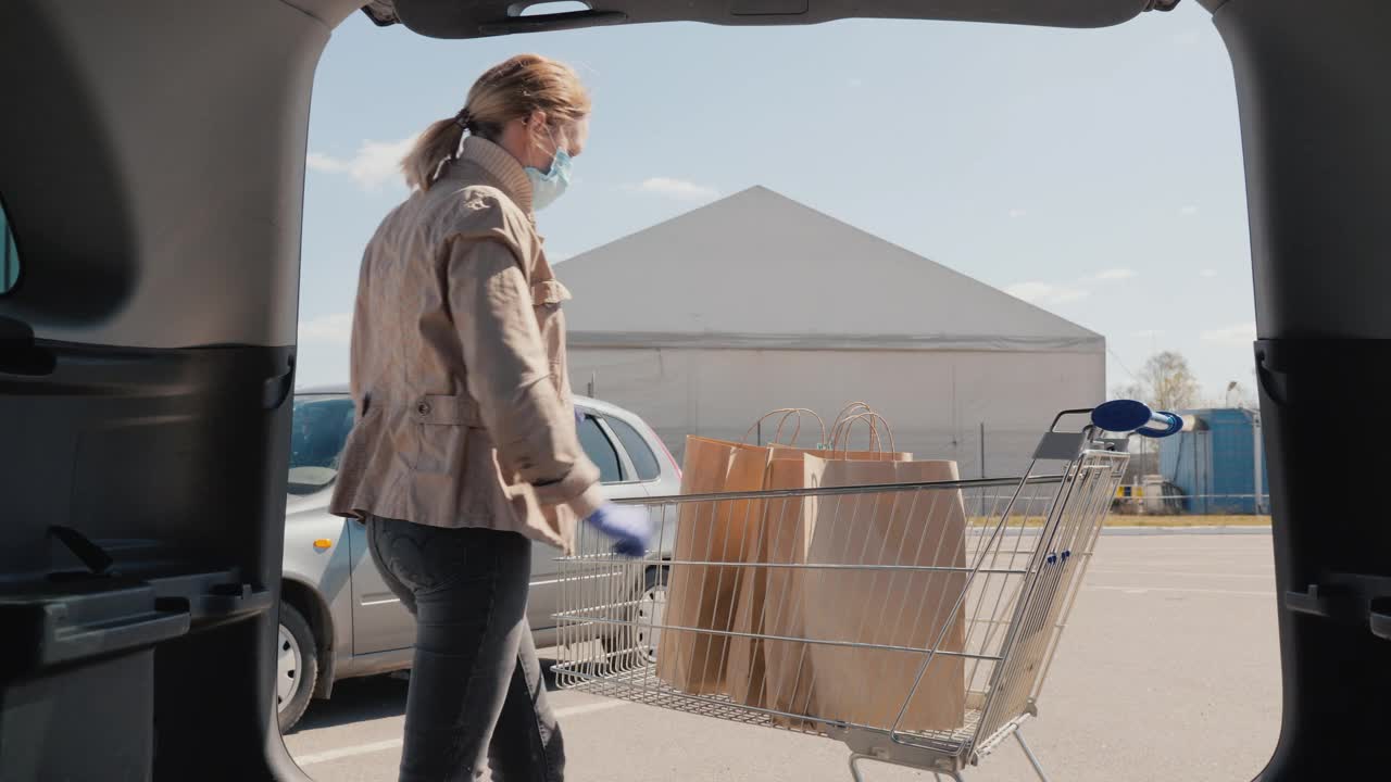 疫情期间的购物——一名妇女把几袋食物放在汽车后备箱里视频素材