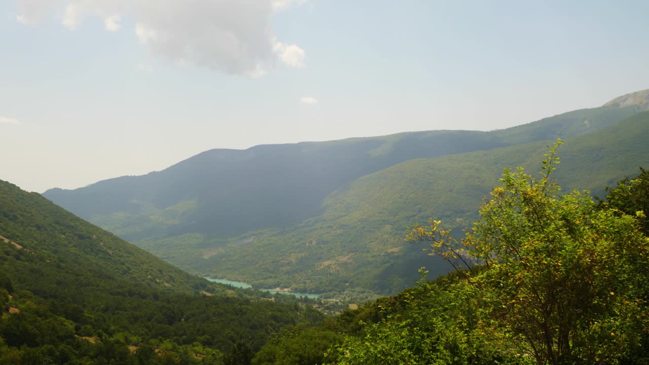 乌云穿过天空，太阳。山脉的背景是绿色的山峰，下面是湖泊和城市。在前面有岩石、草和树的小山上视频素材