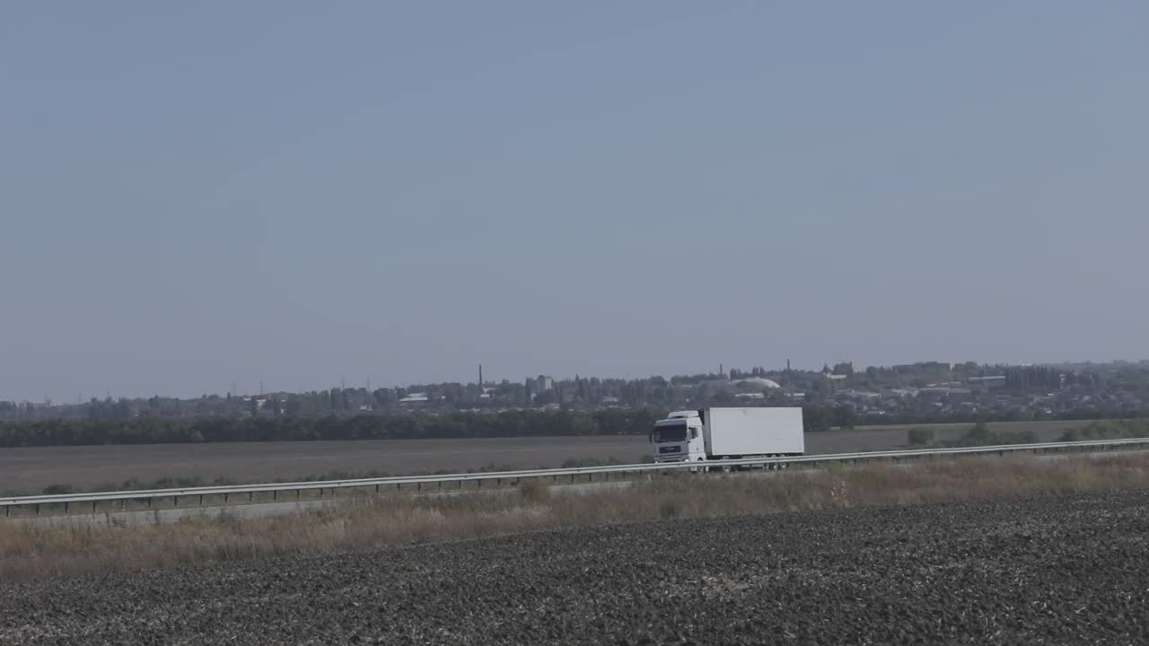 一辆白色的马车在阳光明媚的天气里沿着公路行驶。高速公路上的卡车视频素材