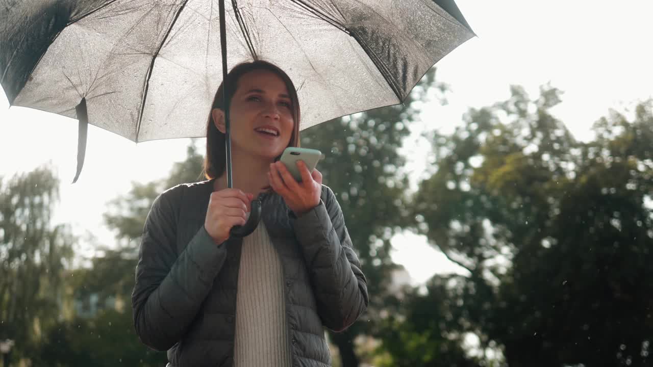 女孩用智能手机语音识别边走边撑着雨伞雨天雨天，口里口里念，晚上语音拨号信息，学生模特年轻上街头语音ai语音信息视频素材