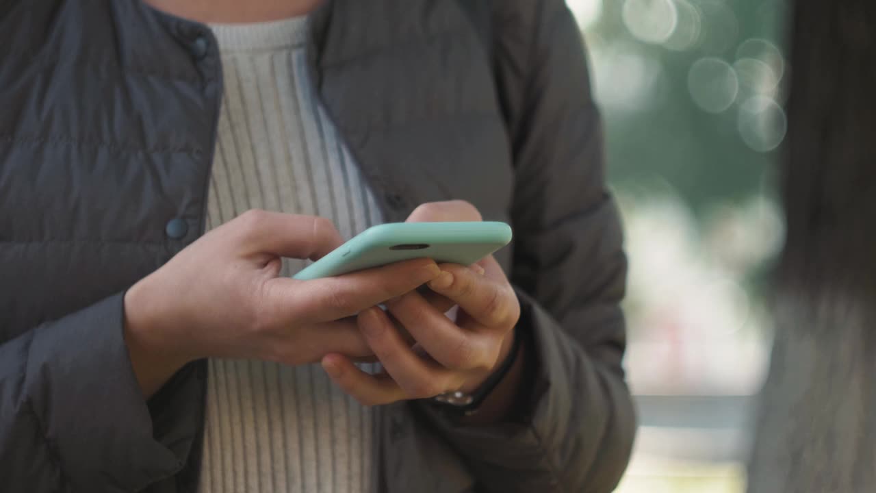 一个时尚快乐的女人的正面视图行走和使用智能手机在城市的街道上，游客走在街道上的日落在小城镇视频素材