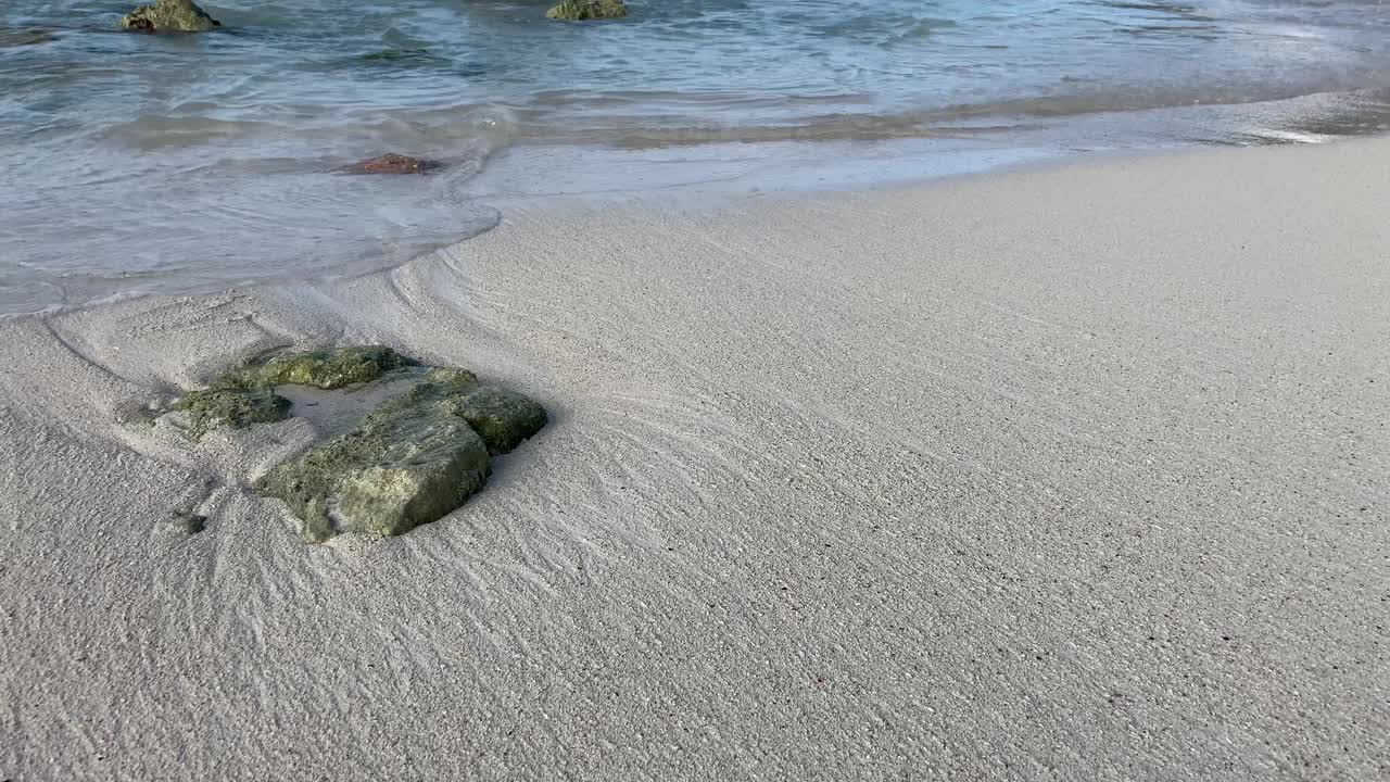 一名男性在潮湿的沙滩上行走，加勒比海浪拍打着裸露的岩石。视频素材