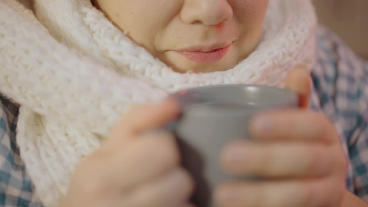 女性戴着白色围巾在家喝热茶，感觉很冷，季节性感染视频素材