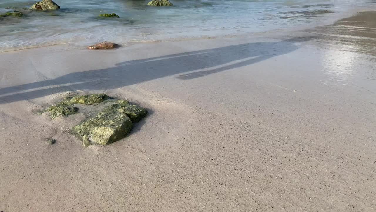 一名男性在潮湿的沙滩上行走，加勒比海浪拍打着裸露的岩石视频素材