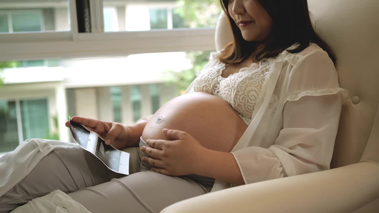 一名亚洲孕妇看着一张超声波婴儿照片视频素材