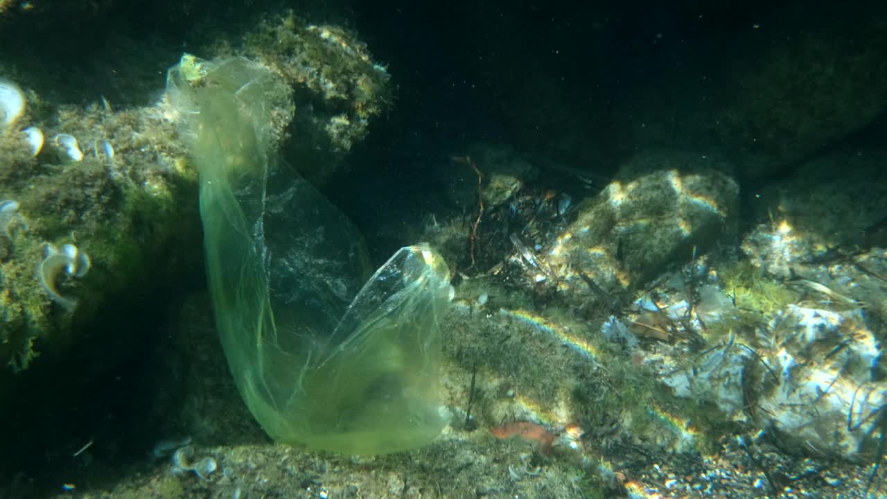 塑料污染，旧的用过的塑料袋躺在石头海床上。水下拍摄视频素材