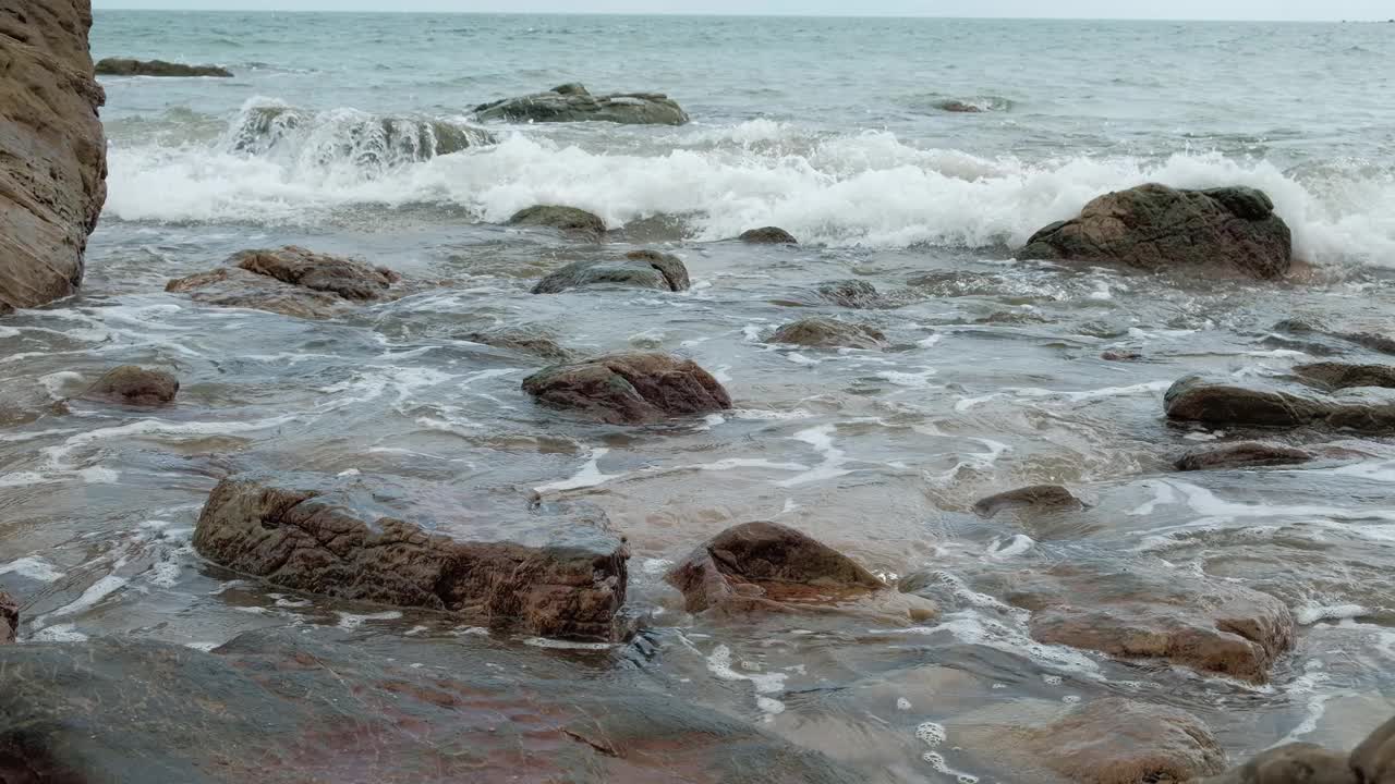 在有许多岩石的海滩上，海浪不停地拍打着海岸。视频素材