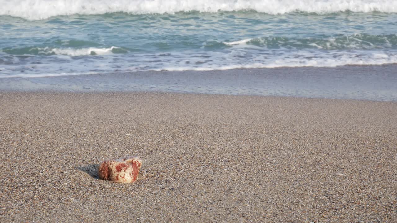 沙滩上的一块石头，平静的海浪在逼近。早上在海滩上。视频素材