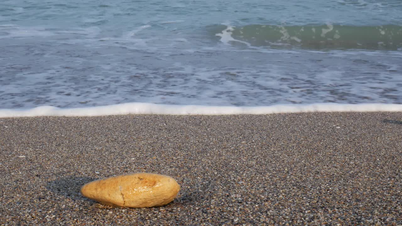 沙滩上的一块石头，平静的海浪在逼近。早上在海滩上。视频素材