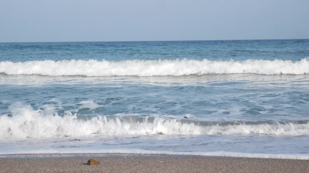 沙滩上平静的蓝色海浪和远处清晨的地平线。未经审查的视频素材