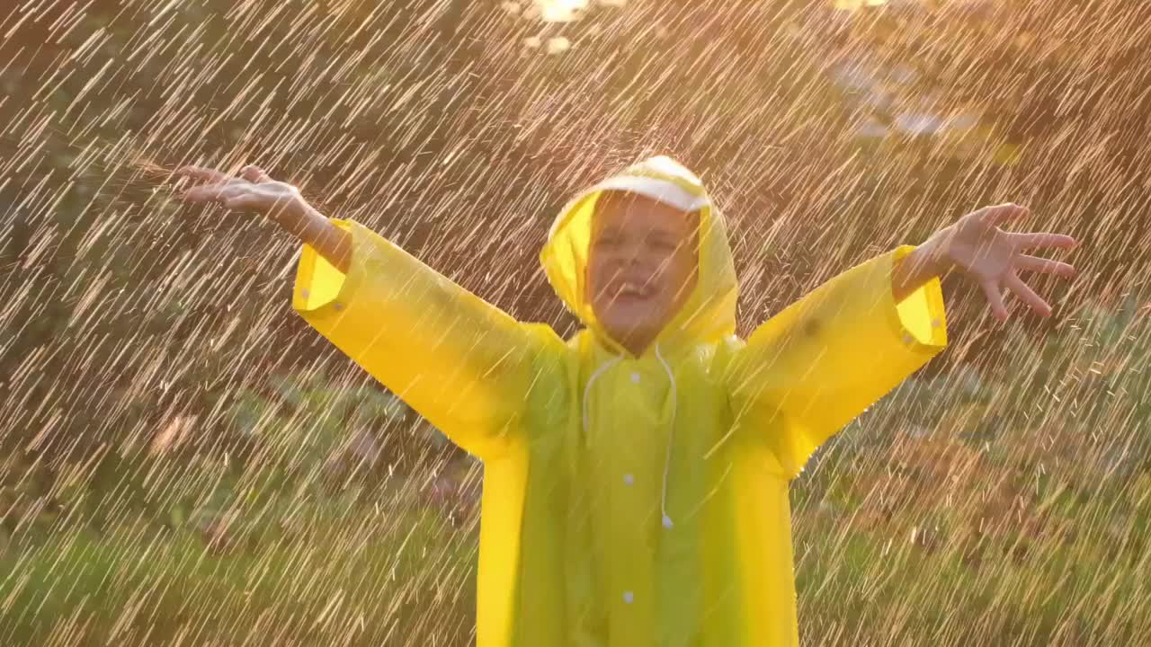 快乐可爱的小男孩微笑着举起双手，穿着黄色雨衣，享受着快乐的雨。孩子们在阳光下玩雨。快乐家庭夏天秋天童年梦想概念120慢莫视频素材