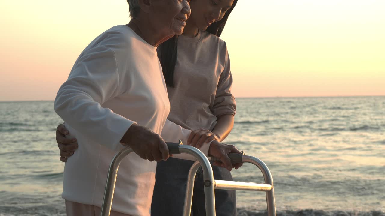 年长的女人和女儿一起在海滩上散步夕阳的背景。视频素材