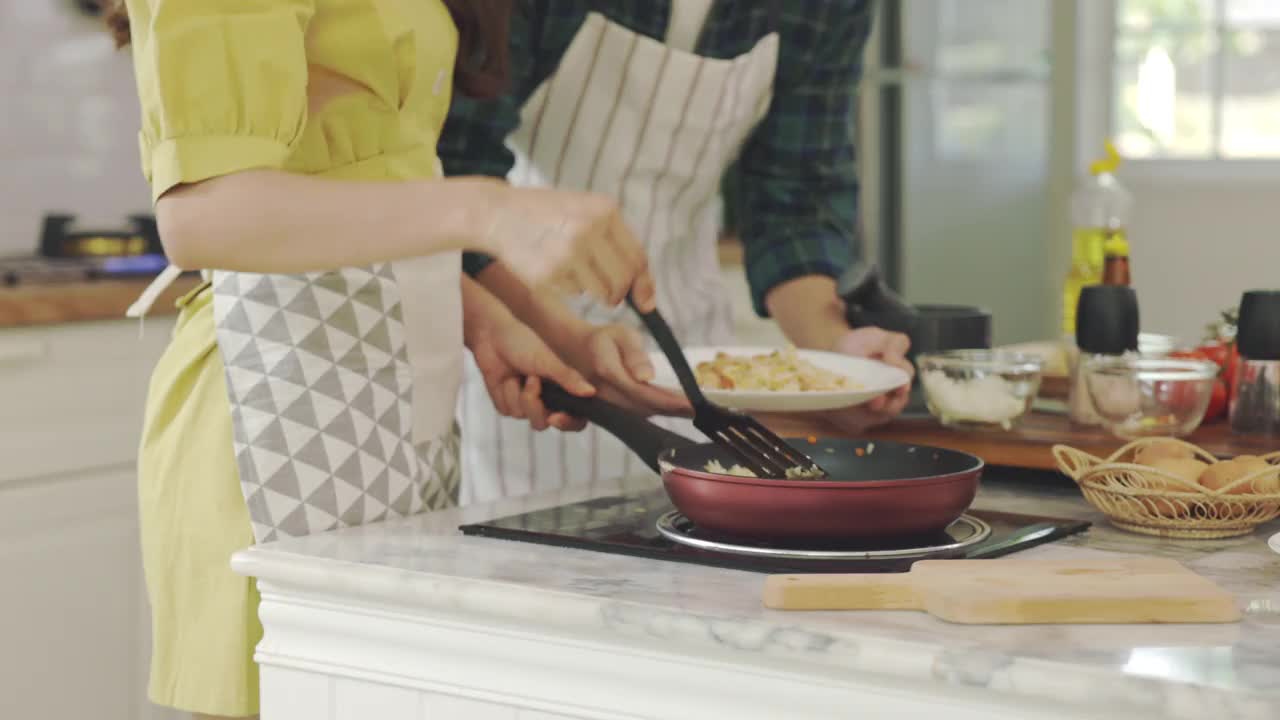 年轻夫妇在家里帮忙做饭，营造浪漫的气氛。在厨房里，情侣们通过帮助对方做早餐来表达爱意。视频素材