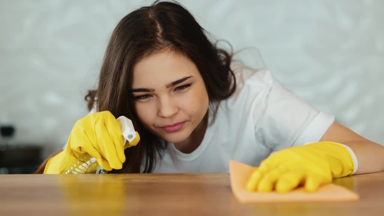 年轻妇女打扫家里。一个黑发的女模特正在厨房里清理一个灶台。女孩听音乐，打扫公寓里的灰尘。慢动作镜头。视频下载