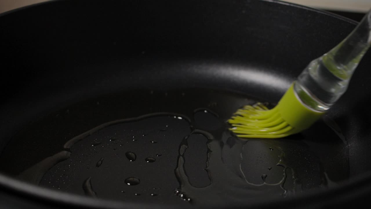 慢镜头男子油脂橄榄油从瓶子到煎锅，特写。微距镜头厨师在煎锅上涂植物油烹饪慢动作。烹饪关闭。视频素材