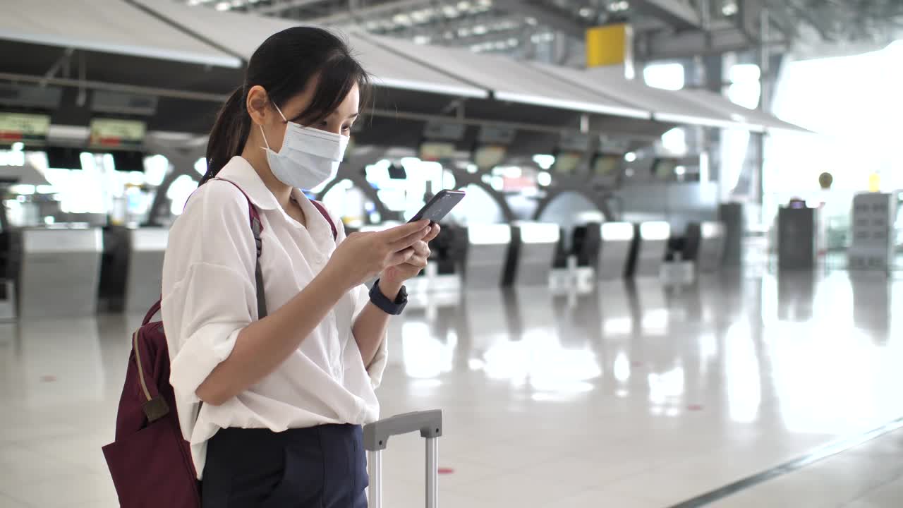 亚洲女性戴着口罩在机场使用智能手机视频素材