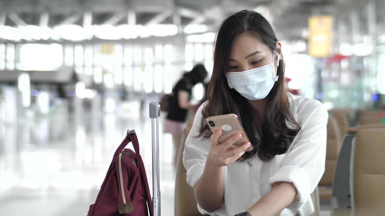 亚洲女性戴着口罩在机场使用智能手机视频素材