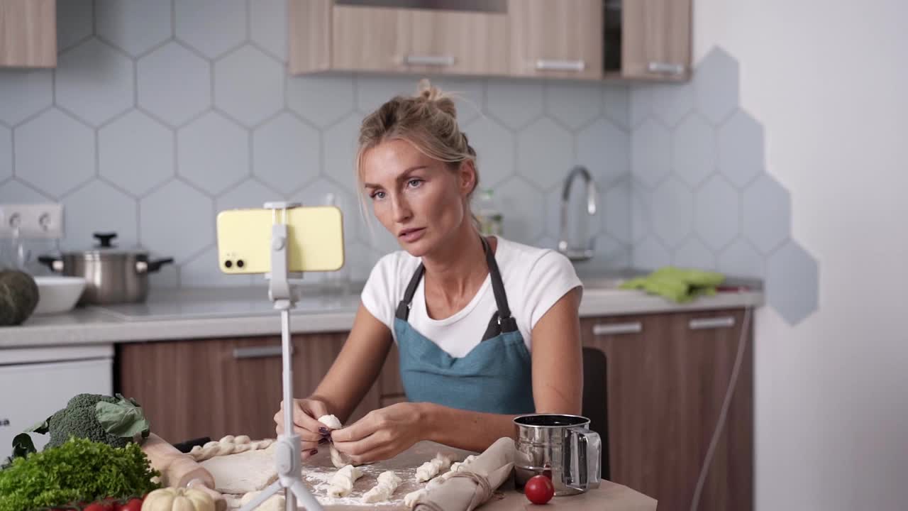 年轻的现代白人妇女正在厨房做饭和看视频菜谱在手机上。视频下载