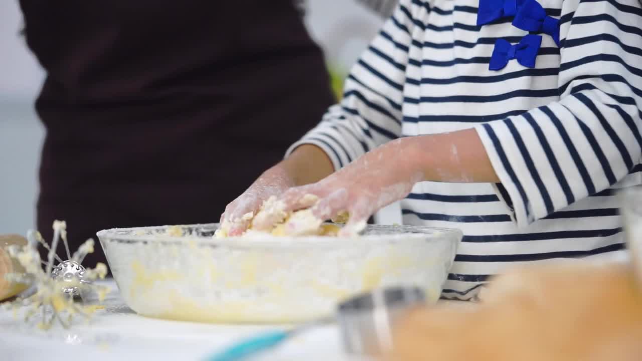 母亲在教女儿在家庭厨房里混合烘焙面团。视频素材