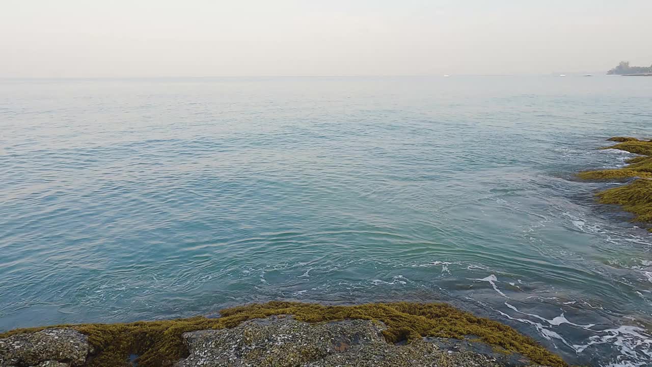 海边蔚蓝的天空、白云和清澈的海水。低潮时阳光透过平静的海浪反射到黑色的岩石上。热带岛屿、海滩、大海，让人耳目一新、放松身心。视频素材