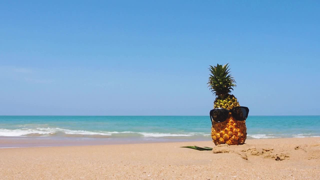 夏日阳光明媚的热带海滩。戴着太阳镜的菠萝在美丽的白色沙滩上。蓝天好不好。在泰国南部的海滩度假。进尺B过路费BG视频素材