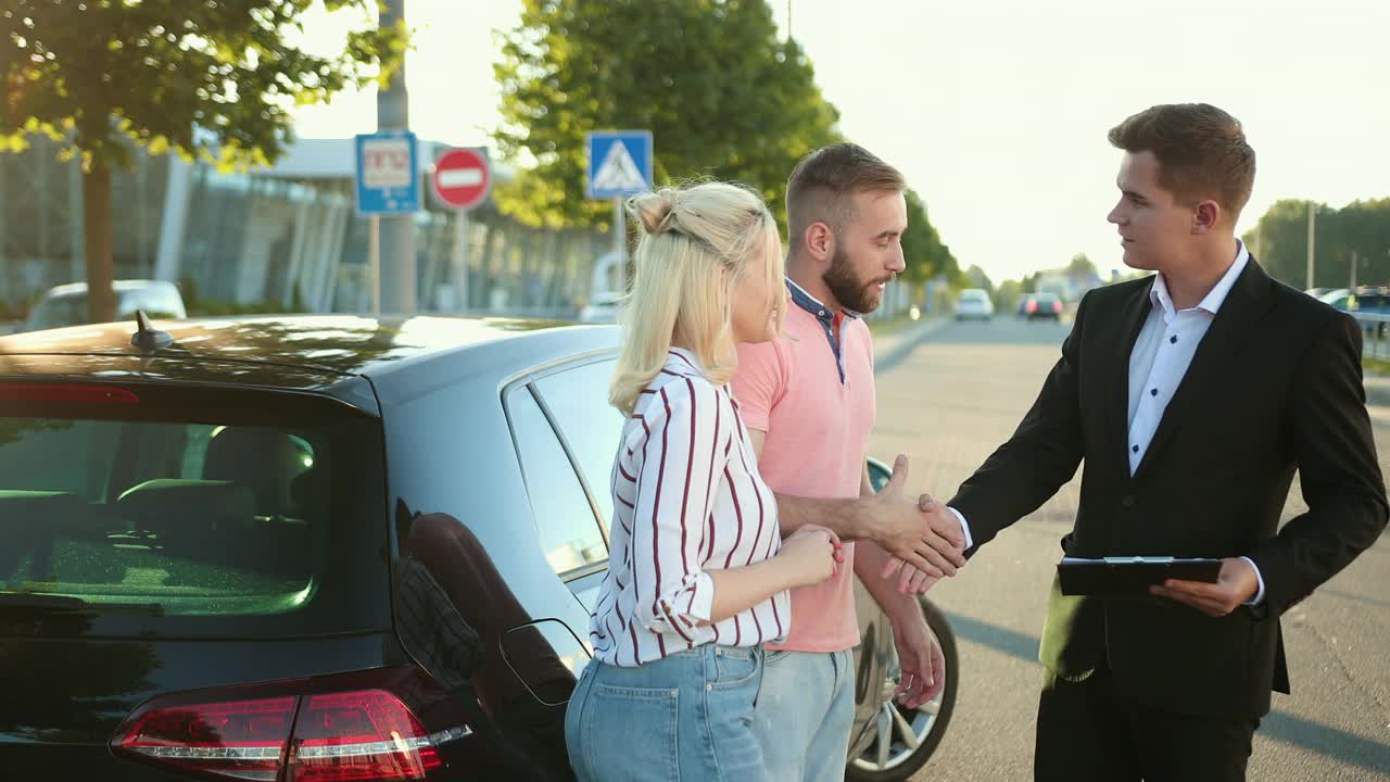 卖家把车卖给了一对幸福的年轻夫妇。男人握着漂亮的车。视频素材