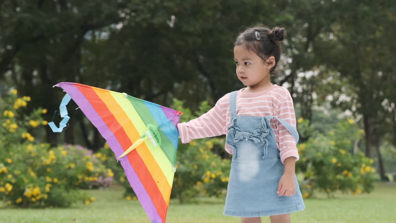 女孩拿着彩虹风筝在公园里旋转。视频素材