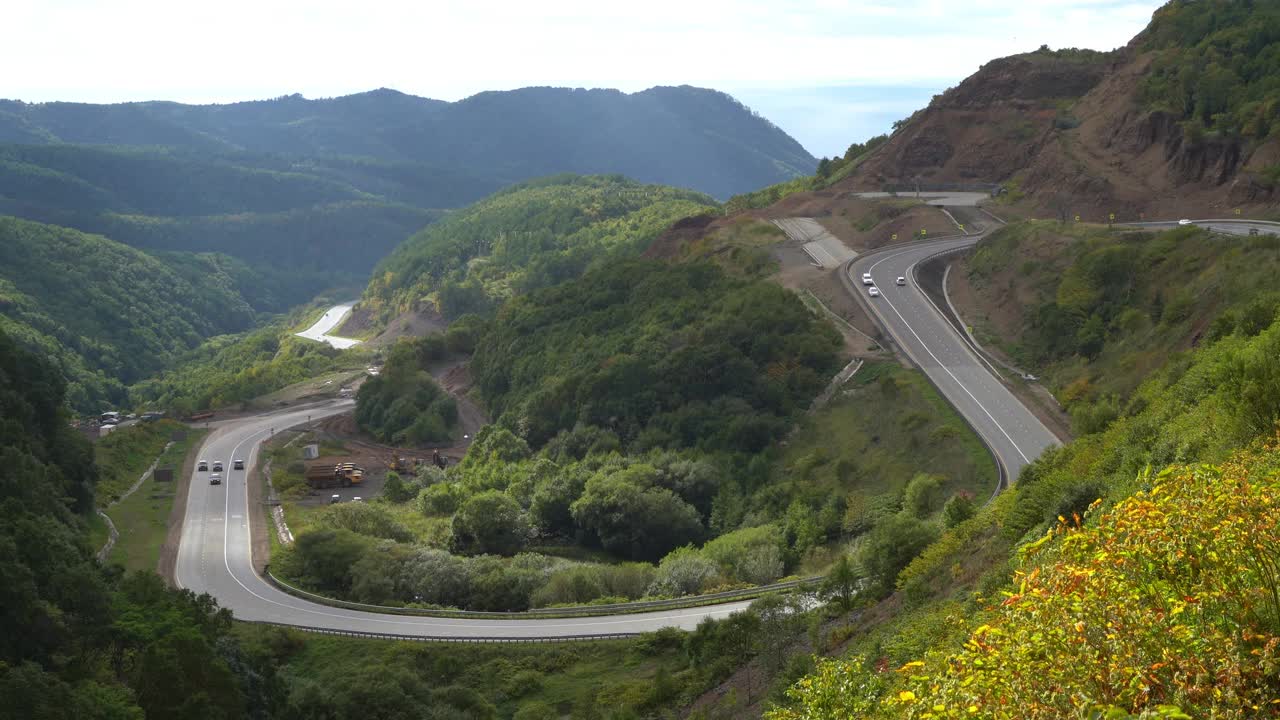 汽车在高原碧绿的山丘上弯弯曲曲的路上行驶视频素材