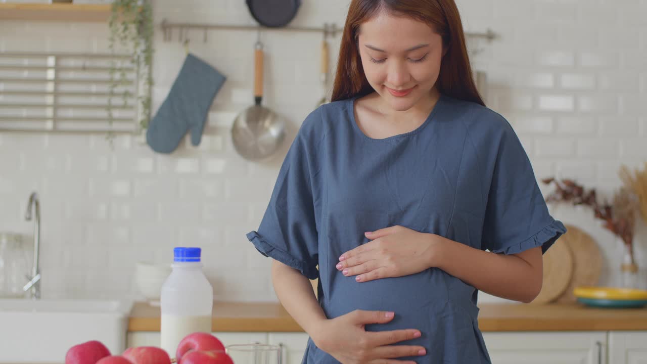 孕妇吃着苹果，轻轻摸着肚子，怀孕/分娩视频素材