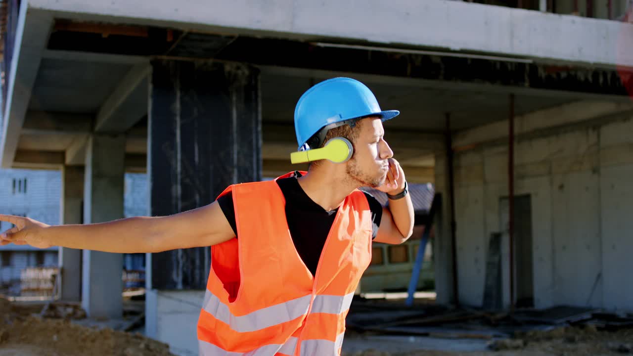 富有魅力的跳舞的建筑工人非洲裔美国人在建筑工地的休息时间听着耳机里的音乐跳舞视频素材