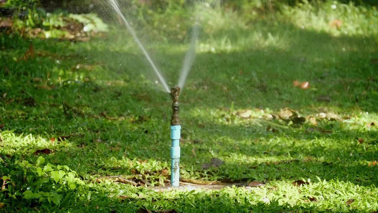 慢镜头拍摄在早晨有阳光的公园里浇草，供水的概念。视频素材