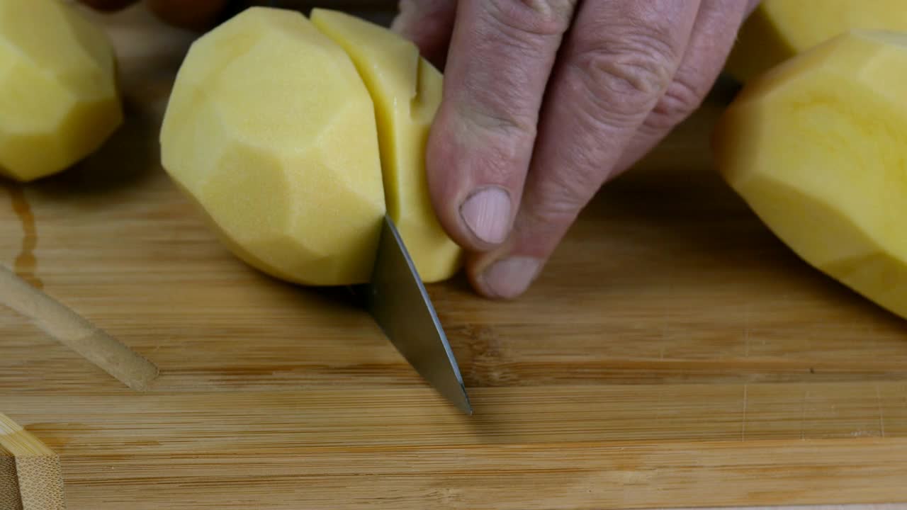 厨师用菜刀将生土豆切成大块，用于制作土豆泥或其他食物。视频素材