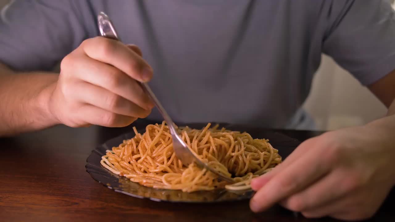 一个男人从一个黑色盘子里拿着番茄酱吃意大利面，特写视频素材