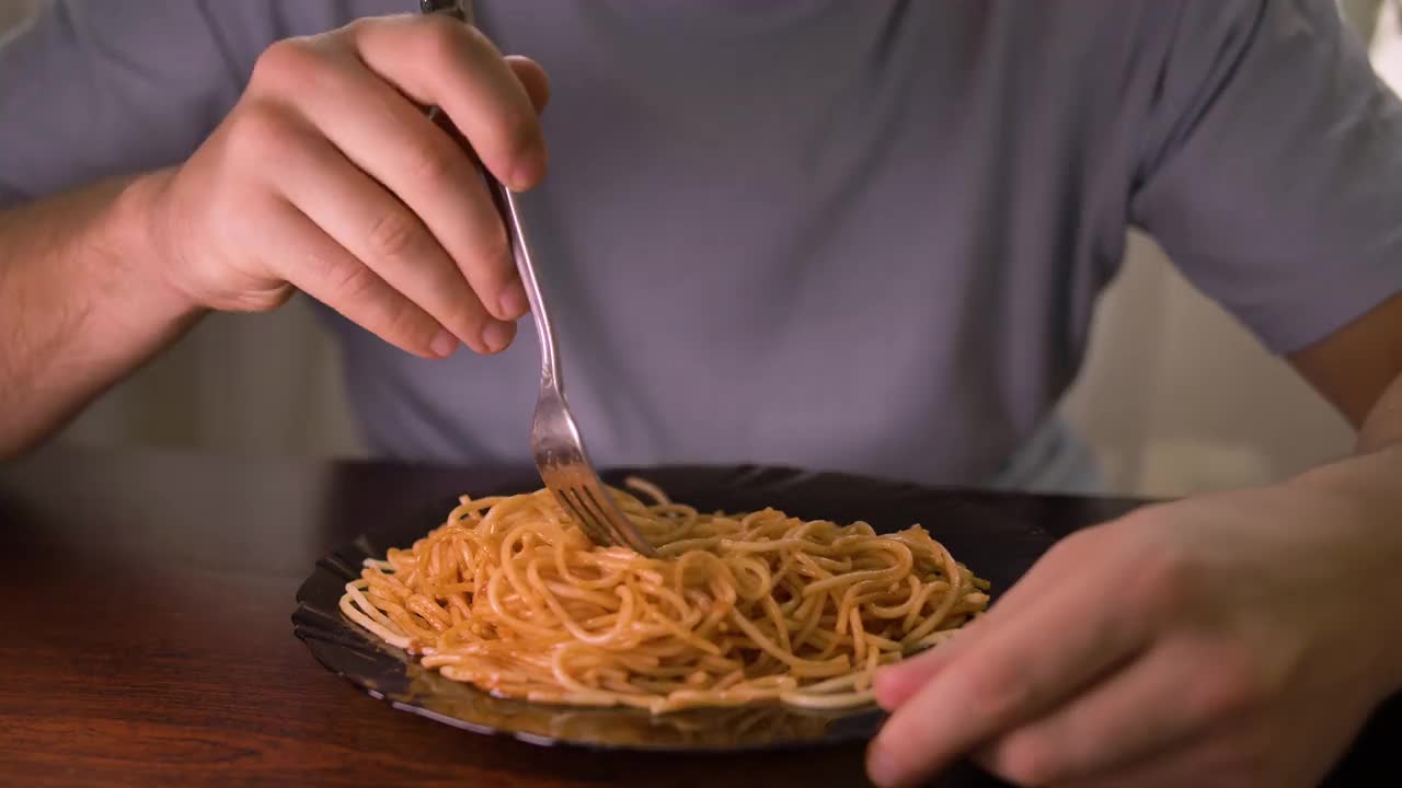 一个男人将意大利面和番茄酱混合在一个黑色盘子里，特写视频素材