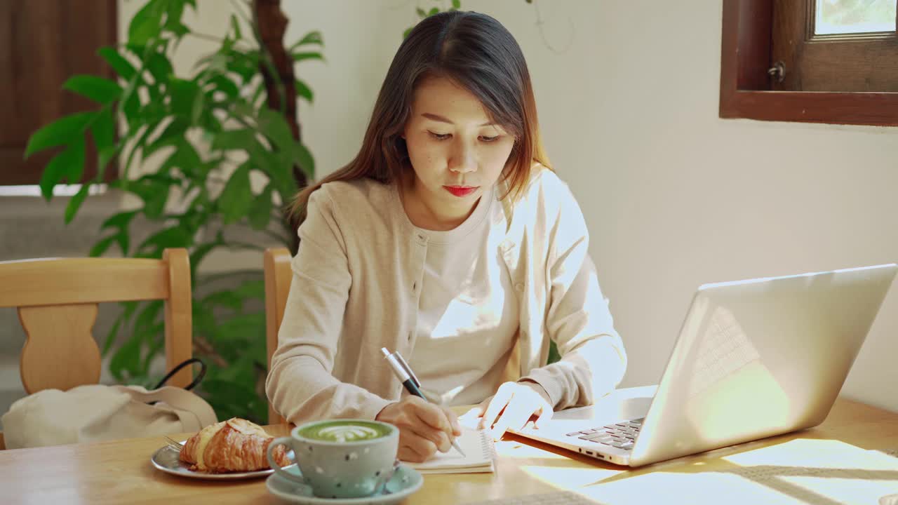 年轻女子拿着一杯咖啡坐在咖啡店里用笔记本电脑工作视频素材