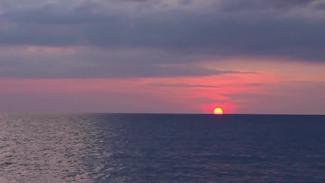 时间流逝b-roll的日落在海洋。五彩缤纷的粉红色天空在雨季。黑压压的云慢慢地移动到红色的太阳落到海里。德龙飞过海面，夕阳如画。自然视频素材