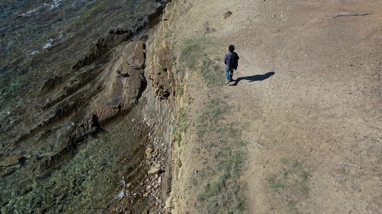 男孩在海边的悬崖上安详地行走。视频素材