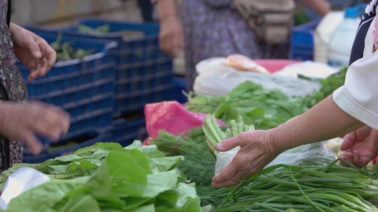 妇女在农贸市场的摊位上购买新鲜的绿色香草。视频素材