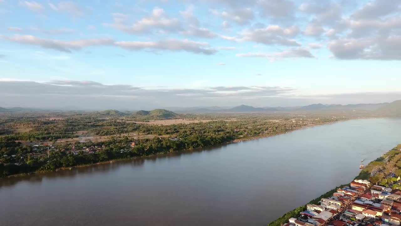 泰国清汗，湄公河的鸟瞰图和河边的村庄，有一条当地的道路经过住宅区，以群山和蓝天为背景视频素材