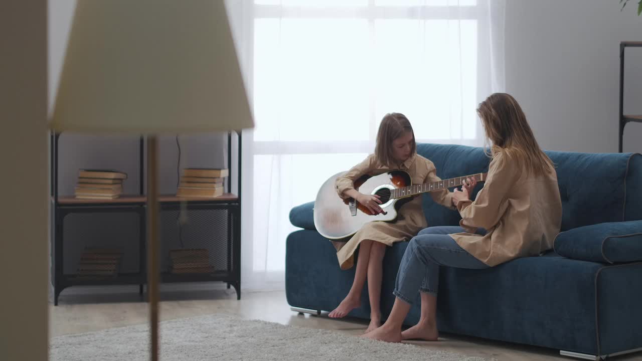 女人和小女儿一起呆在家里，孩子在学弹吉他，女人在帮助她视频素材