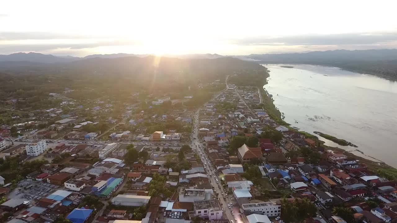 泰国清汗，湄公河的鸟瞰图和河边的村庄，那里有一条当地的道路经过住宅区，背景是群山和天空中的星期天视频素材