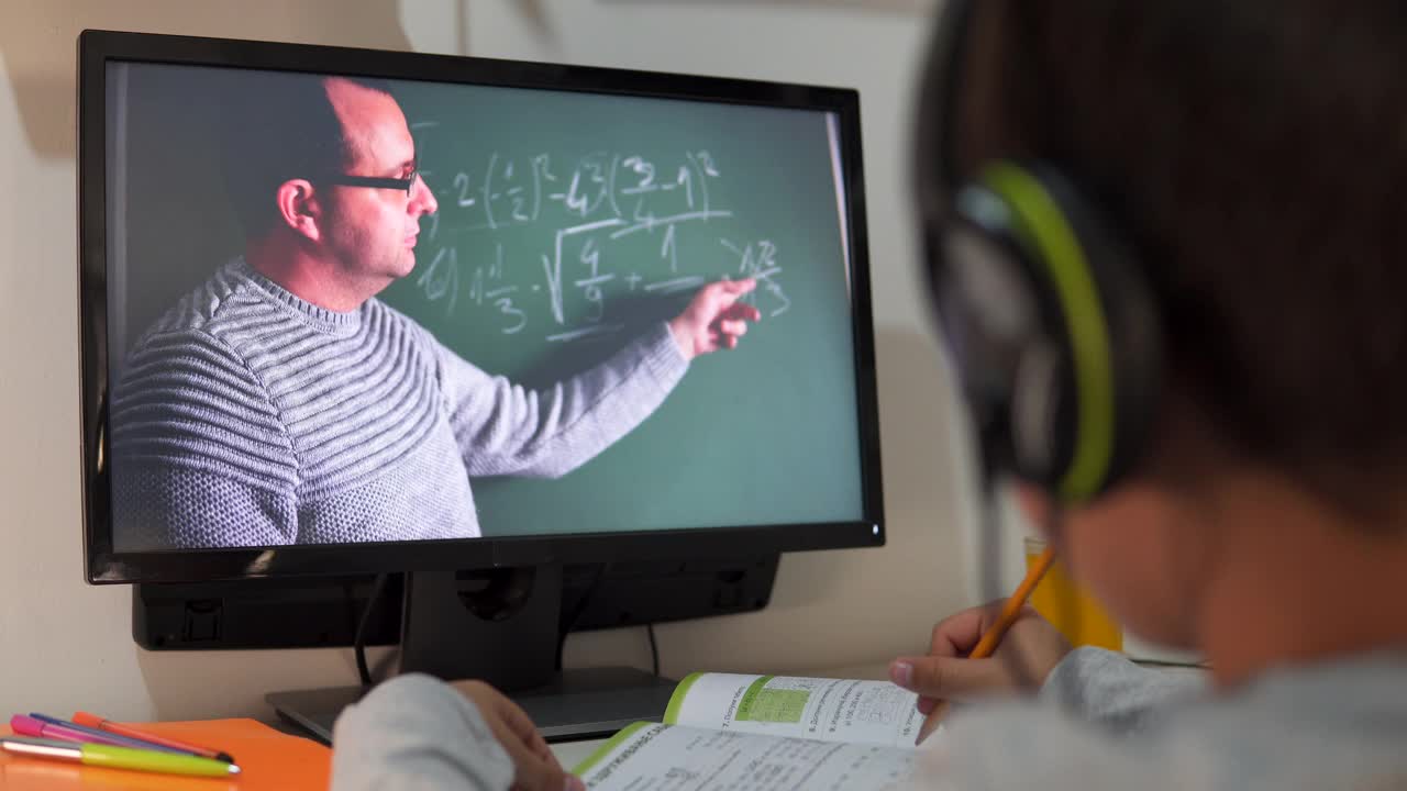 远程学习中，一个男孩戴着耳机坐在家里的桌子旁。理念线上教育、家庭教育、科技、学校视频素材