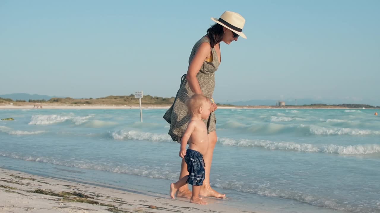 女人在海边享受家庭周末。母亲和儿子走在海边。视频素材