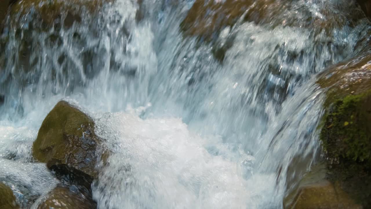 在夏天的森林里，清澈的蓝色的水在潮湿的石头之间流动。视频素材