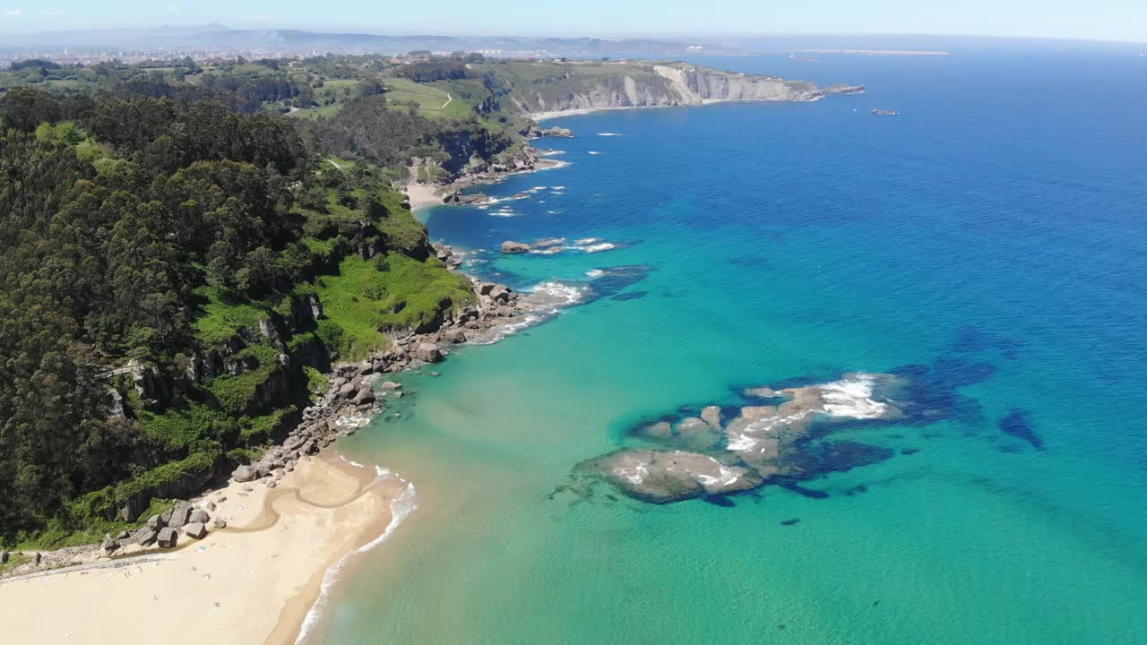 蓝绿色的大海和石崖与郁郁葱葱的绿色植被，La Ñora海滩，Villaviciosa, Gijón，阿斯图里亚斯，西班牙。视频素材