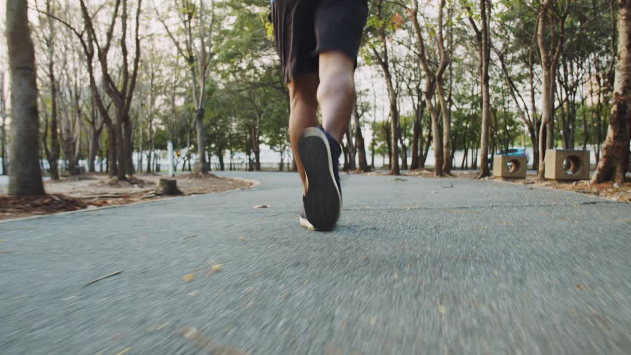 低角度拍摄近距离腿年轻男子跑步锻炼在一个美丽的日落公园。视频素材