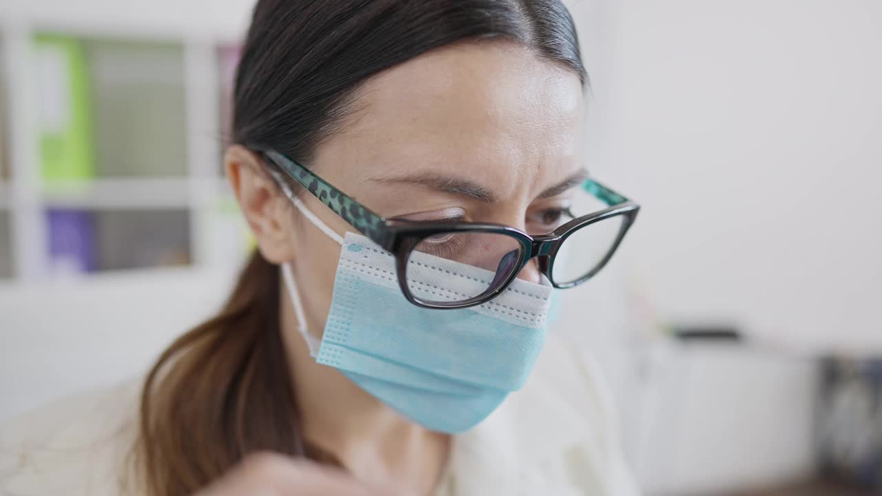 年轻苗条女子在2019冠状病毒病口罩下摘掉雾蒙蒙眼镜的大头照。办公室应对新冠肺炎疫情工作不便。室内白人女员工的特写视频素材